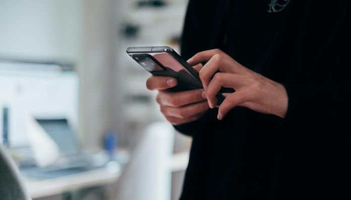 angedeutete Person, die ein handy bedient mit Büro im Hintergrund