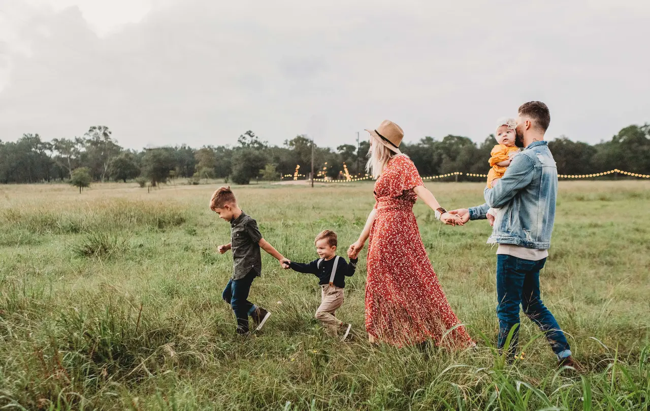 Familie mit drei Kindern geht Hand in Hand über eine Wiese. 