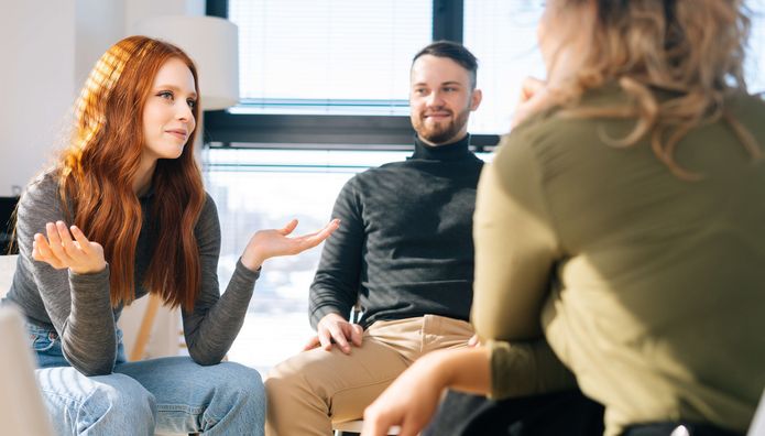 Young successful coworkers sitting on chairs in circle, discussing working or personal issues together.