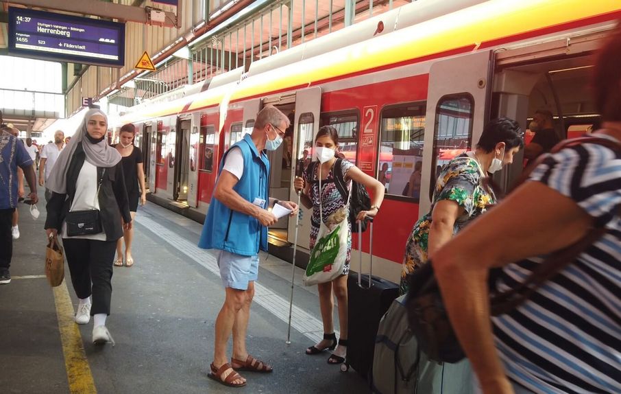 Ein Ehrenamtlicher der Bahnhofsmission hilft einer jungen Frau beim Umsteigen.